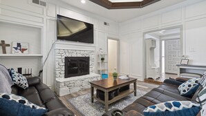 A living room with a stone fireplace, a flat-screen TV, leather sofas, and a wooden coffee table. - Family friendly/POOL/Sleeps 16/Luxury (Plano)
