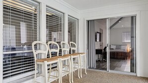 A room with a dining area featuring white chairs with wooden seats, a table, and large windows with blinds. There is a sliding glass door leading to a bedroom with a bed and a desk. - Family friendly/POOL/Sleeps 16/Luxury (Plano)