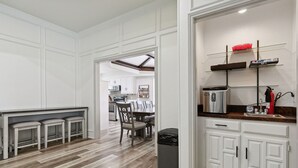A modern kitchen with white cabinetry, a wooden countertop, and a built-in oven. There is a dining area with a table and chairs visible in the background. - Family friendly/POOL/Sleeps 16/Luxury (Plano)