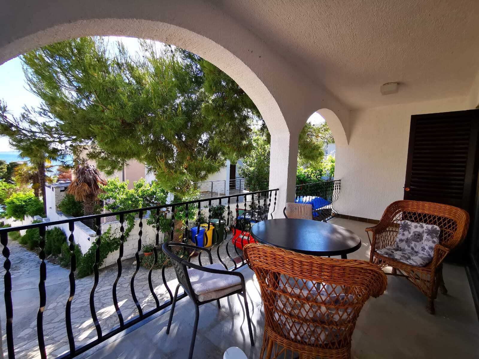 A balcony with a table and chairs, a railing, and a view of greenery and buildings.