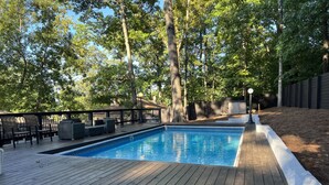 A rectangular swimming pool with a wooden deck, surrounded by trees and a fence. - LOCATION - DUNWOODY; NEW-BEAUTIFUL MODERN HOUSE & Outdoor Seasonal Private Pool (Atlanta)