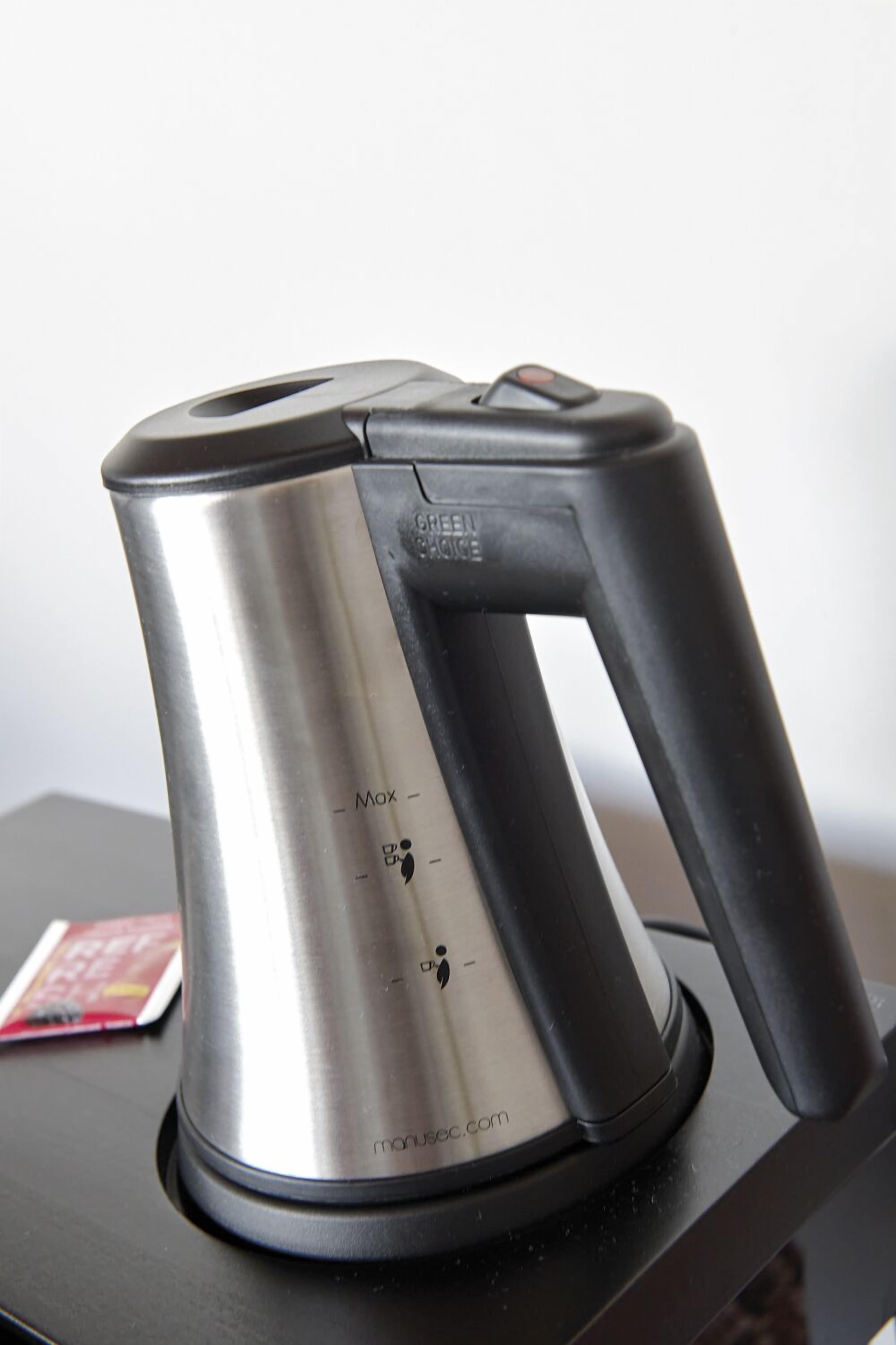 A stainless steel electric kettle with a black handle and a base, placed on a black surface.