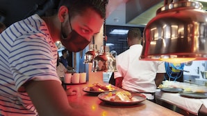 Een kok bereidt eten in een keuken met roestvrijstalen apparatuur en hangende koperen pannen.