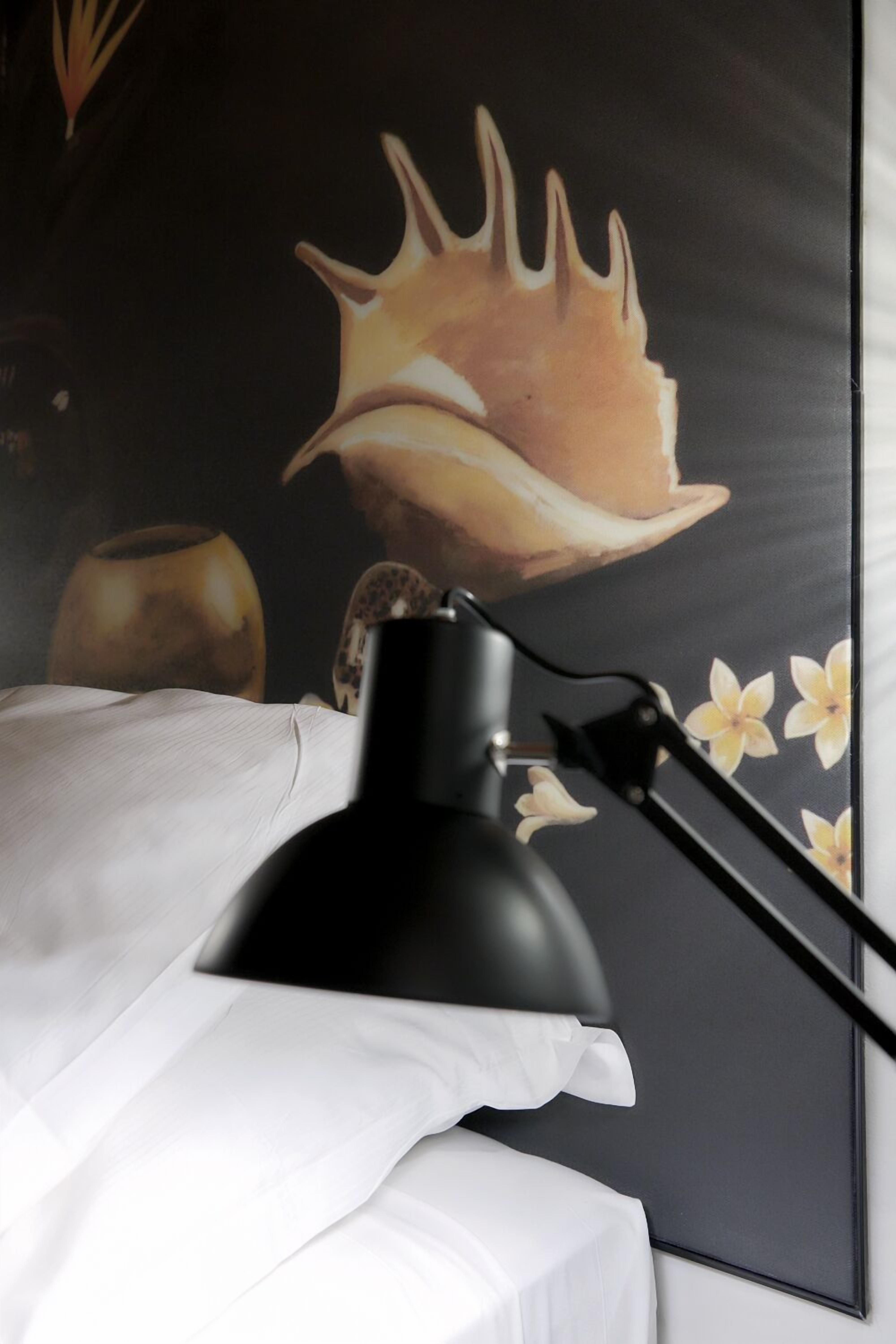A bed with white linens, a black desk lamp, and a wall with a seashell and floral design.