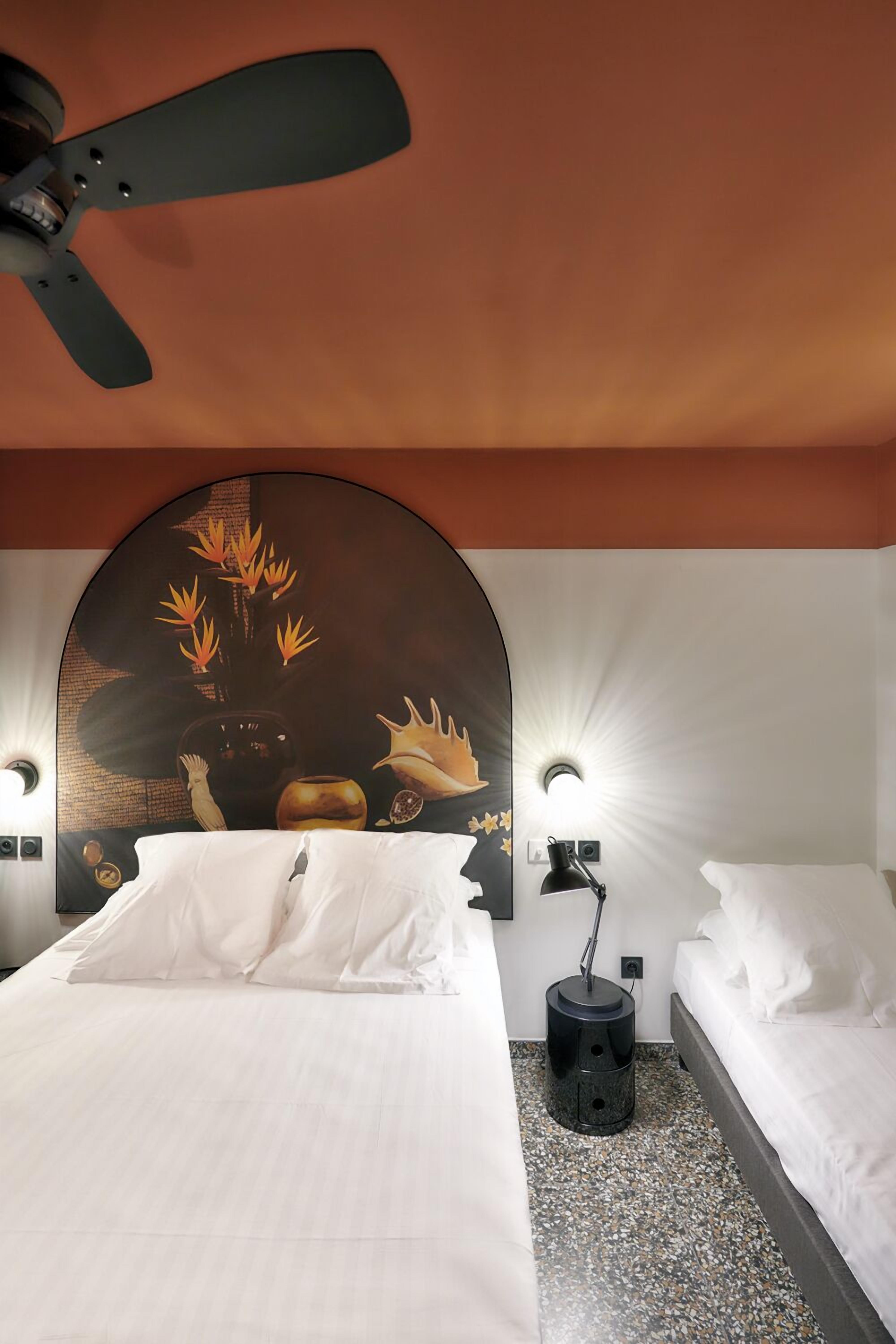 A hotel room with a bed, a ceiling fan, a wall-mounted light, and a decorative headboard.