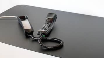 A modern desk with a telephone and a coiled cord.