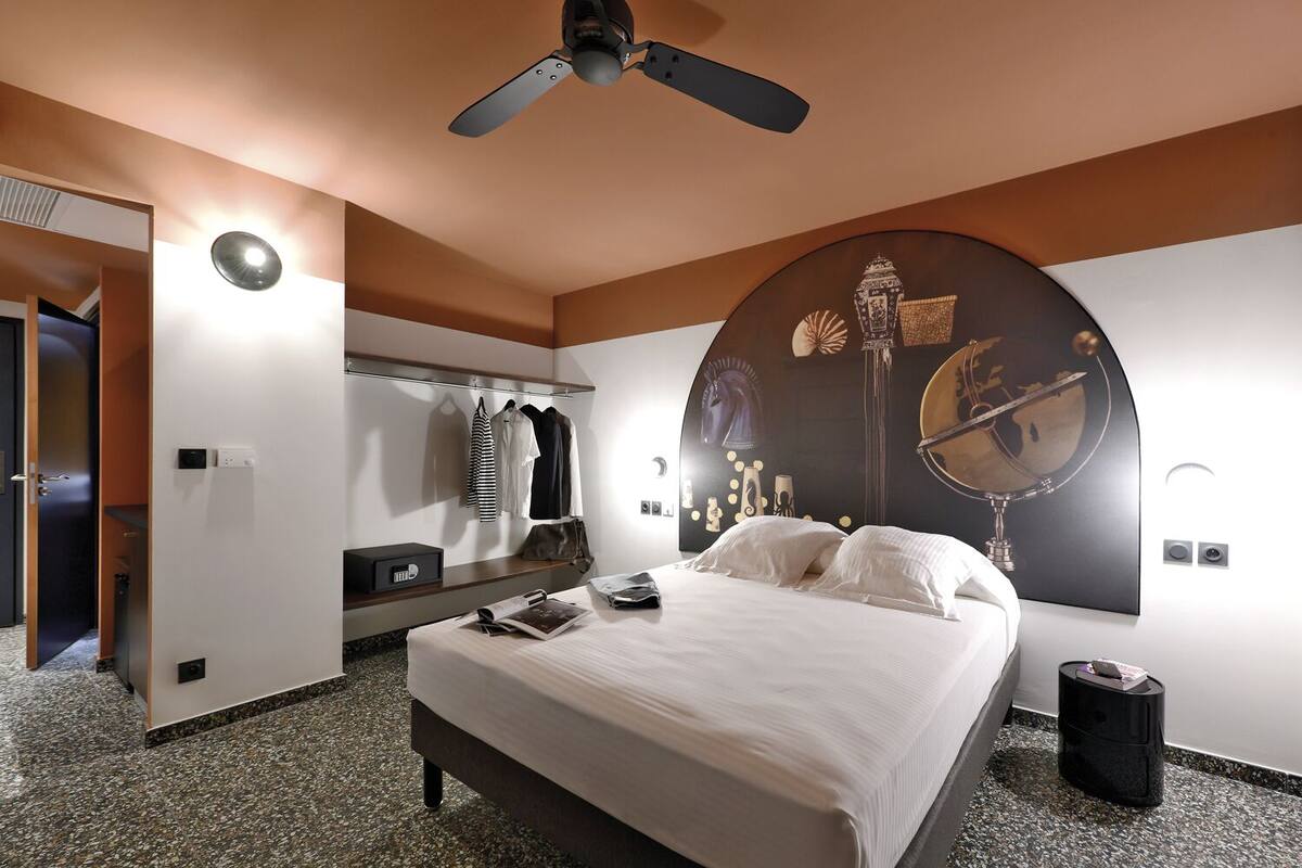 Een moderne hotelkamer met een bed, een plafondventilator, een grote spiegel en een kledingkast.