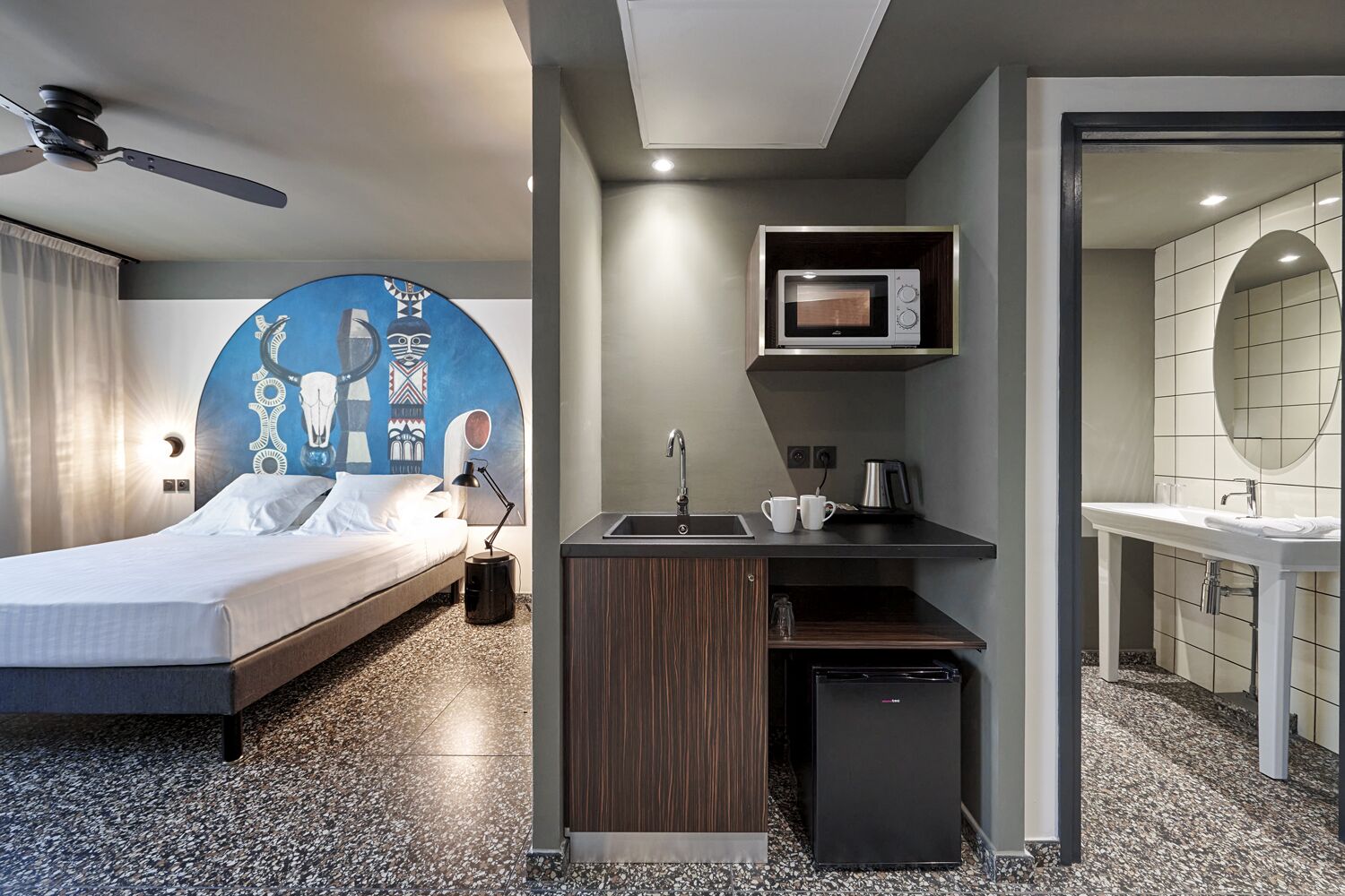 Een moderne hotelkamer met een bed, een klein keukentje, een badkamer en een unieke muurdecoratie.