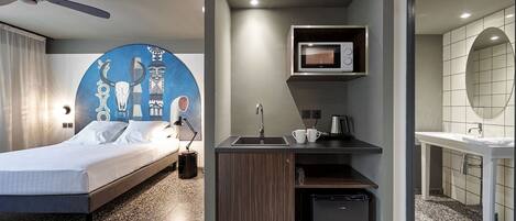 A modern hotel room with a bed, a small kitchenette, a bathroom, and a unique wall mural.