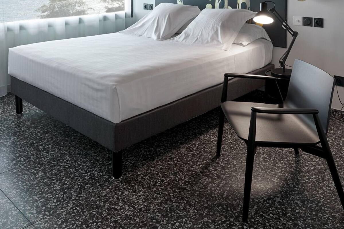 Een moderne hotelkamer met een bed, een bureau, een stoel, een plafondventilator en een groot raam met uitzicht op zee.