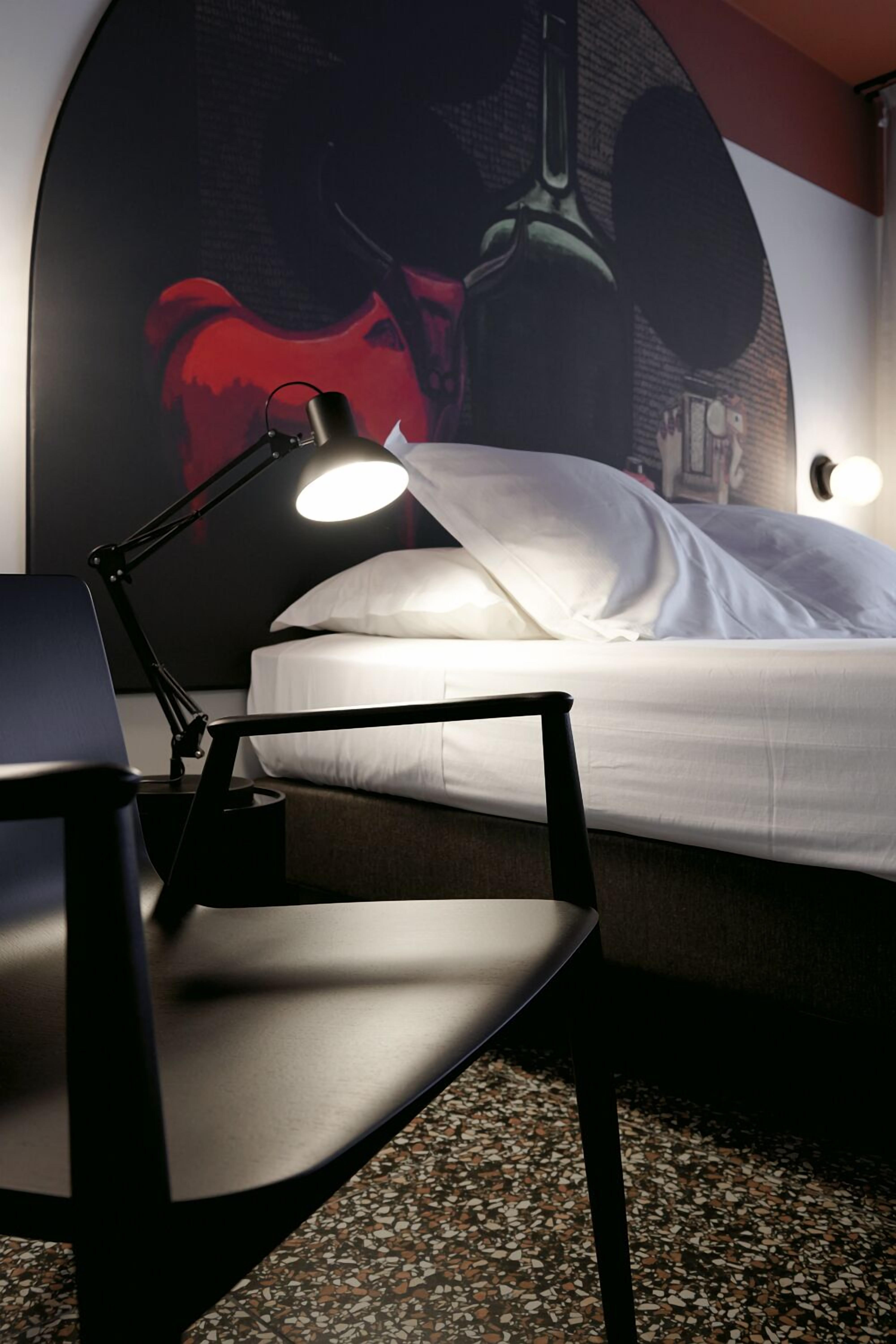 A neatly arranged hotel room with a bed, a desk with a lamp, and a wall with a large poster.