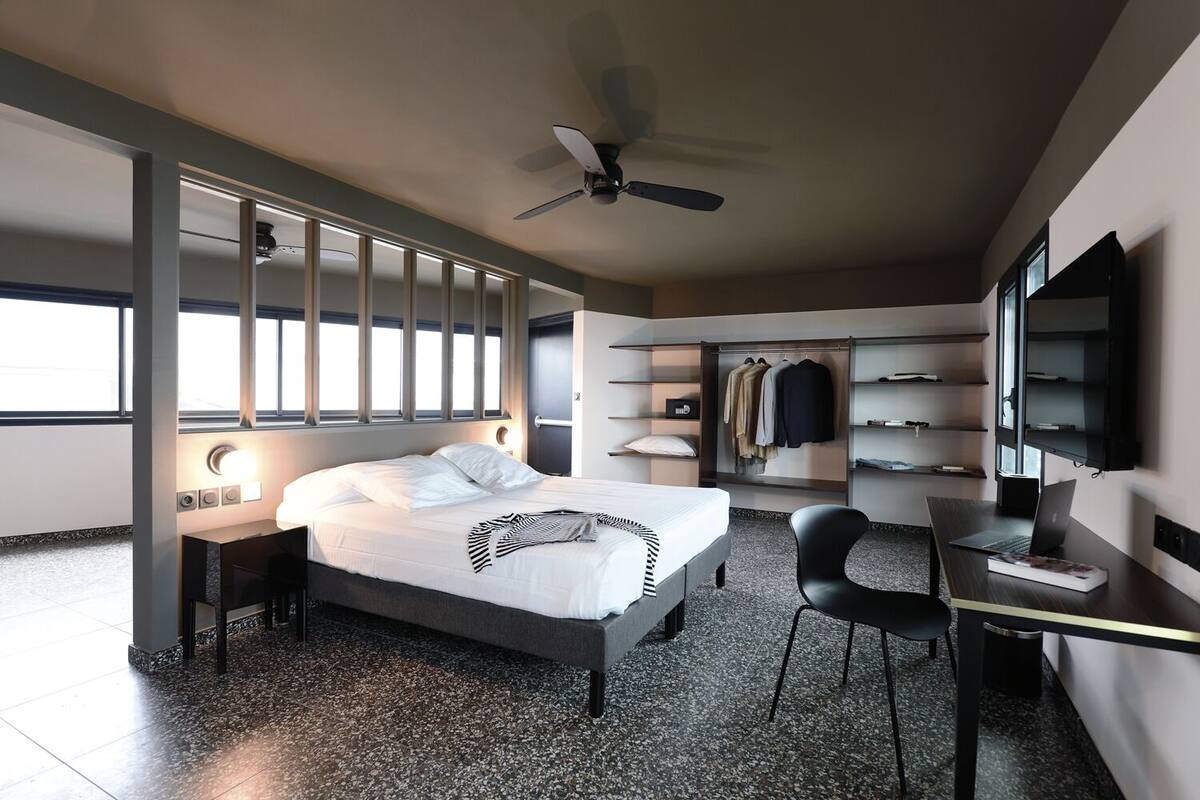 Een moderne hotelkamer met een bed, bureau, stoel, kledingkast en plafondventilator.