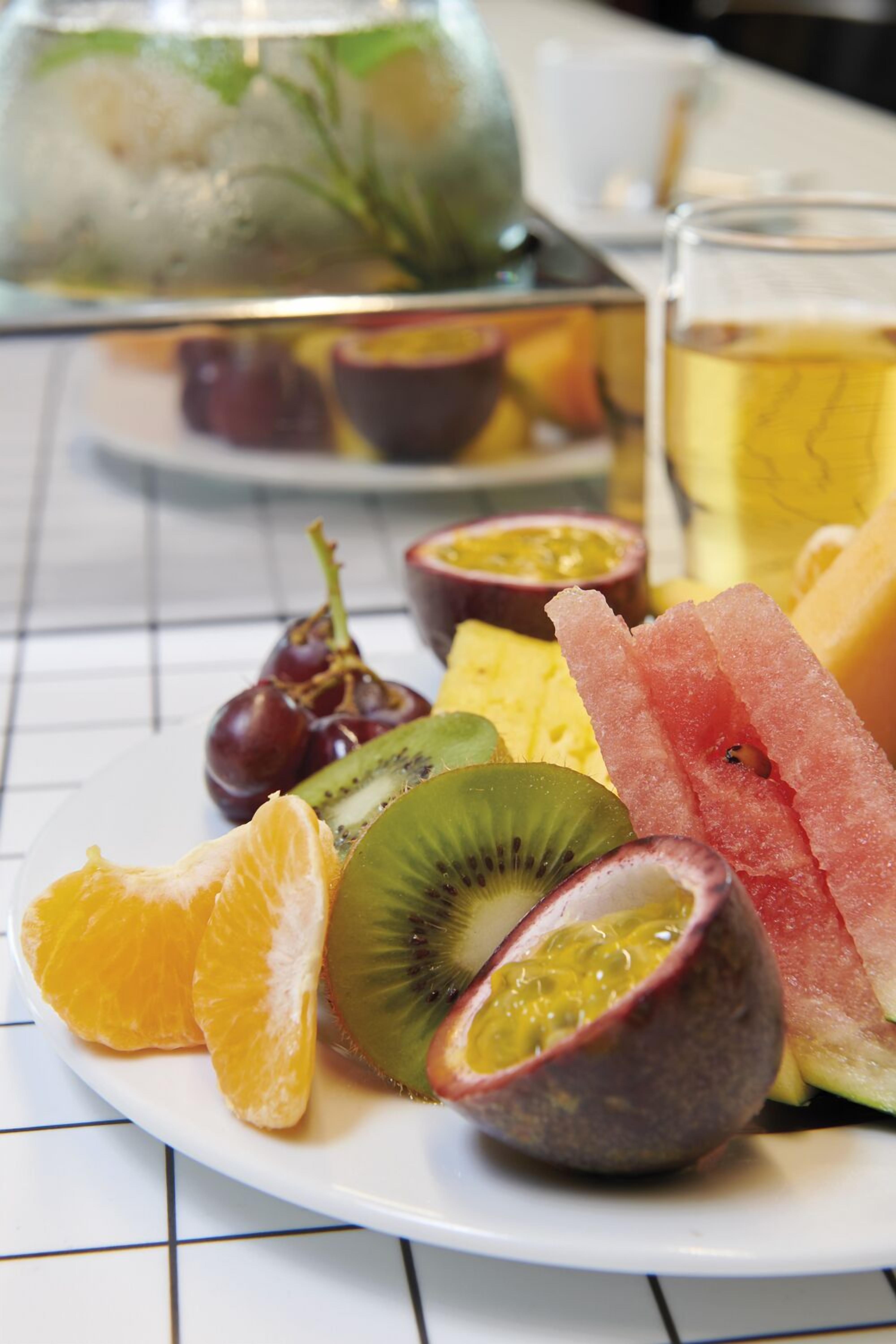 Un plato de frutas variadas, como kiwi, maracuyá y sandía, con un vaso de té helado al fondo.
