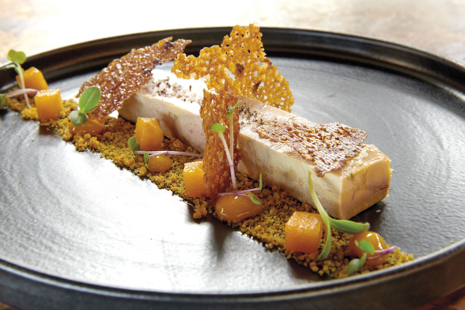 A dish with a piece of meat, garnishes, and a textured base on a plate.