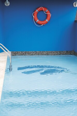 Une piscine avec un escalier en métal et un bouée de sauvetage rouge fixée au mur.
