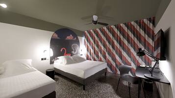 Una habitación de hotel con una cama, un escritorio con una silla, un ventilador de techo y una pared con un diseño a rayas.
