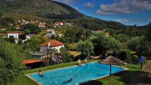 A swimming pool surrounded by lush greenery and houses in a hilly area. - Toca dos Lobos - Ecological Cabin (Caminha)
