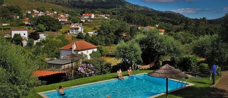 A swimming pool surrounded by lush greenery and houses in a hilly area.