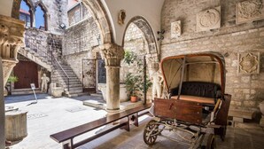An interior courtyard with stone arches, a wooden carriage, and a bench. - Deluxe Room in Hotel Rose Split (Split)