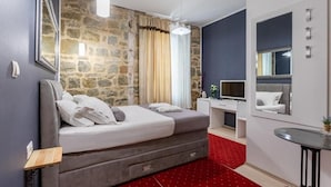 A bedroom with a bed, a desk, a chair, a TV, and a mirror. - Castle View in Deluxe Room - Hotel Rose Split (Split)