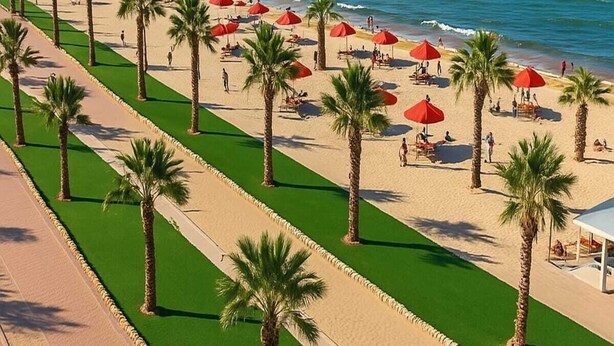 A beach with palm trees, red umbrellas, and a clear blue sky. - Luxurious Chalet With Stunning Views in Port Said, Egypt (Al-Manasrah)