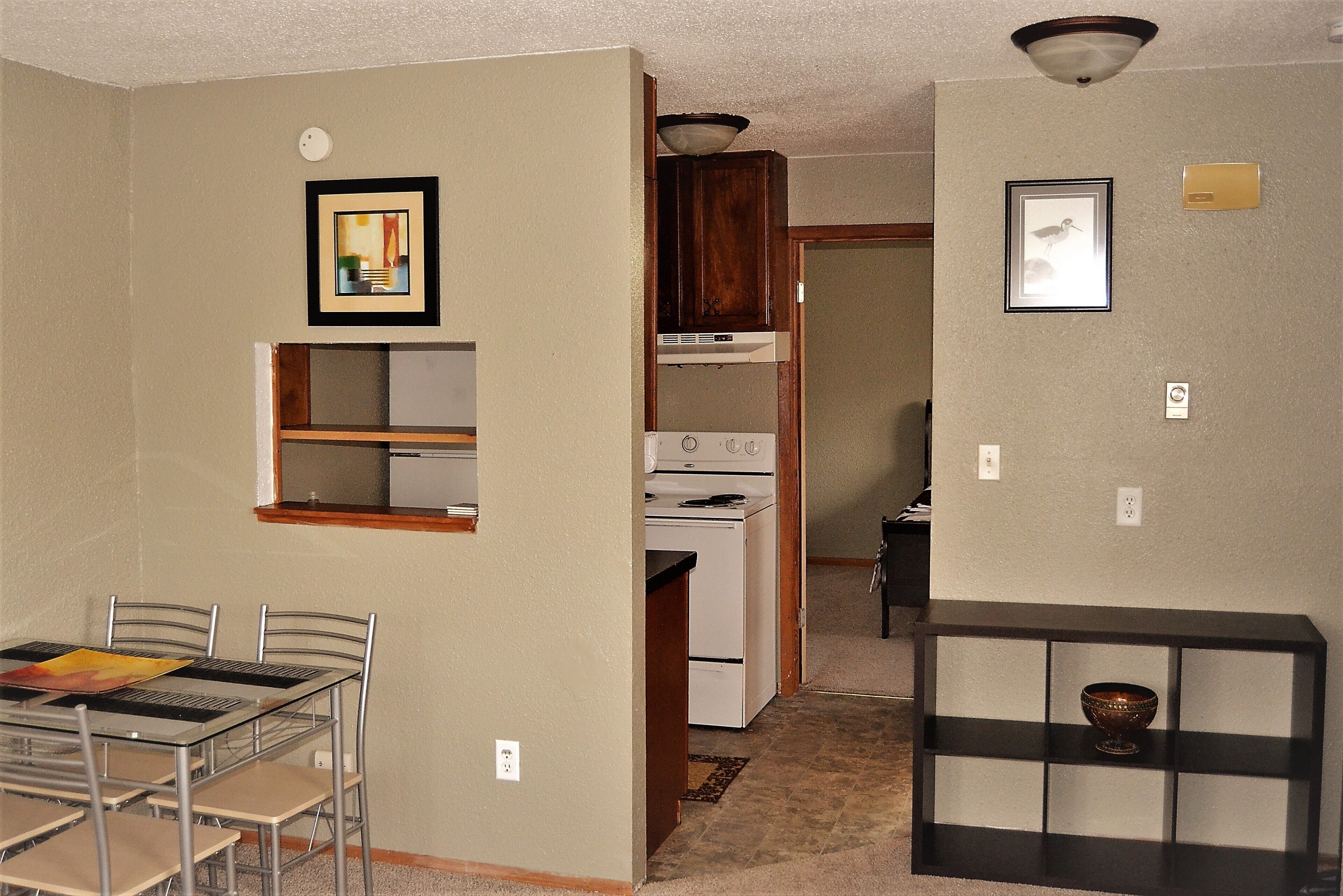 A kitchen with a stove, cabinets, and a dining area with chairs and a table.