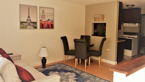 Ein Wohnzimmer mit einer Couch, einem Esstisch mit Stühlen, einer Lampe und einer Küchenzeile mit Schränken und einer Mikrowelle.