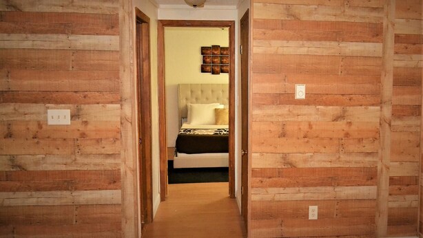 Ein schmaler Flur mit Holzwandverkleidung, einem Bett mit Kopfteil und einer kleinen Wanddekoration.