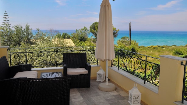 A balcony with wicker furniture, a white umbrella, and a view of the sea. - Holiday House Angelos C on Agios Gordios Beach (Corfu)