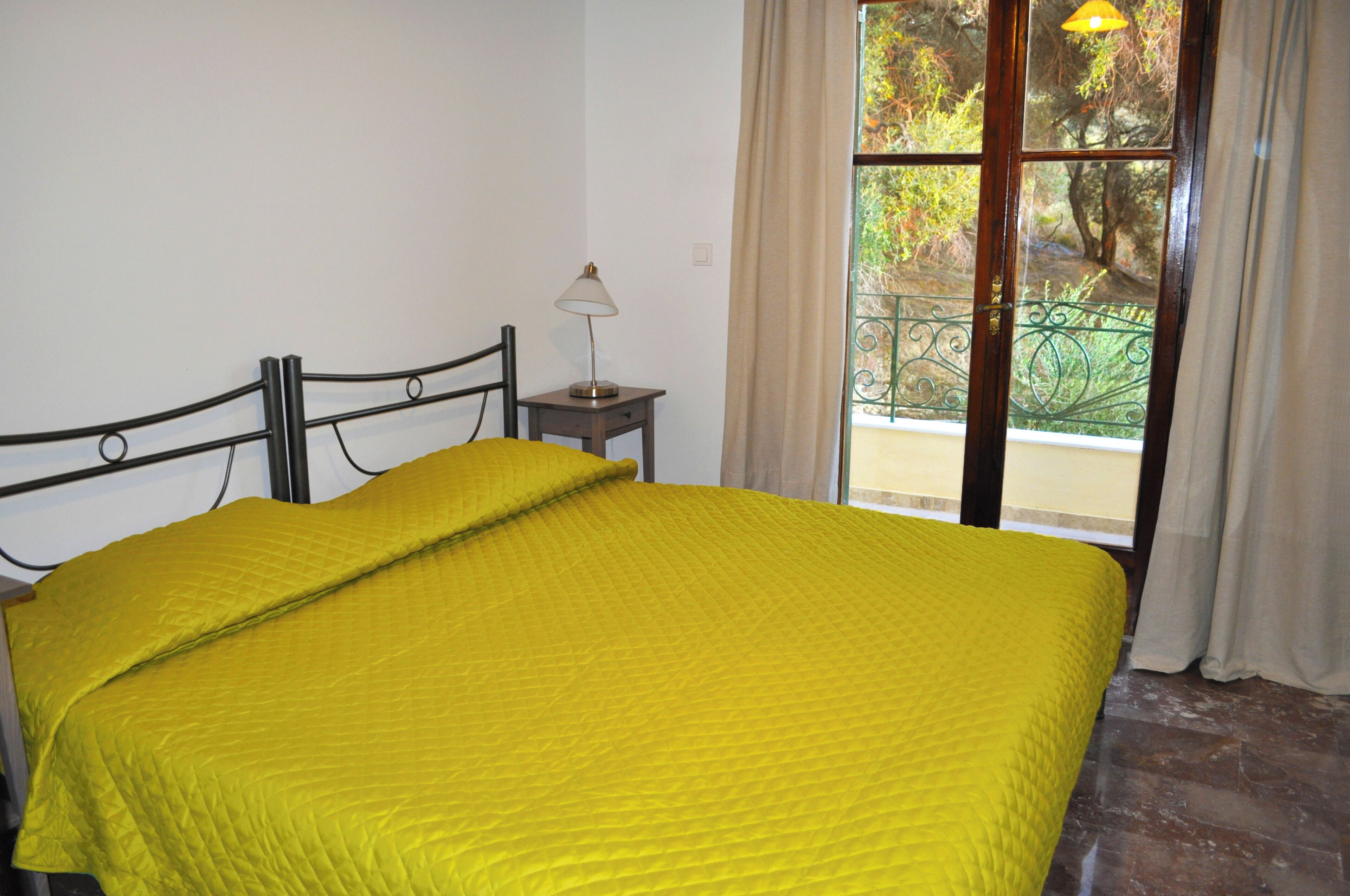 A room with a bed, a nightstand, a lamp, and a window with curtains.