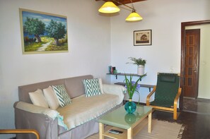 A living room with a sofa, a glass coffee table, a chair, a painting, and a door.