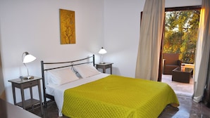 A bedroom with a bed, two bedside tables with lamps, a painting on the wall, and a view of the outdoors. - Holiday House Angelos C on Agios Gordios Beach (Corfu)