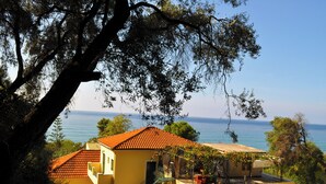 A yellow building with a red-tiled roof, a staircase, and a view of the sea. - Holiday House Angelos on Agios Gordios Beach (Corfu)