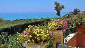 A coastal view with a clear sky, a body of water, and a variety of colorful flowers in pots. - Holiday House Angelos on Agios Gordios Beach (Corfu)