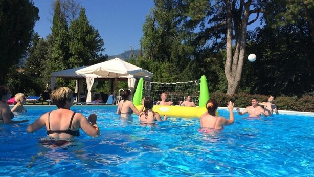 Uma piscina com pessoas, uma tenda e árvores ao fundo.