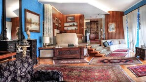 Quarto com parede azul, painéis de madeira, sofá, poltrona, mesa e estante.