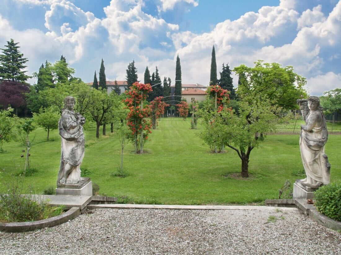A garden with statues, a lawn, and a building in the background.