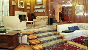 Uma sala de estar com lareira, painéis de madeira, um sofá branco e uma escada.