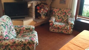 Ein Wohnzimmer mit Kamin, floralen Sesseln, einem Flachbildfernseher und einem Fenster mit Aussicht.