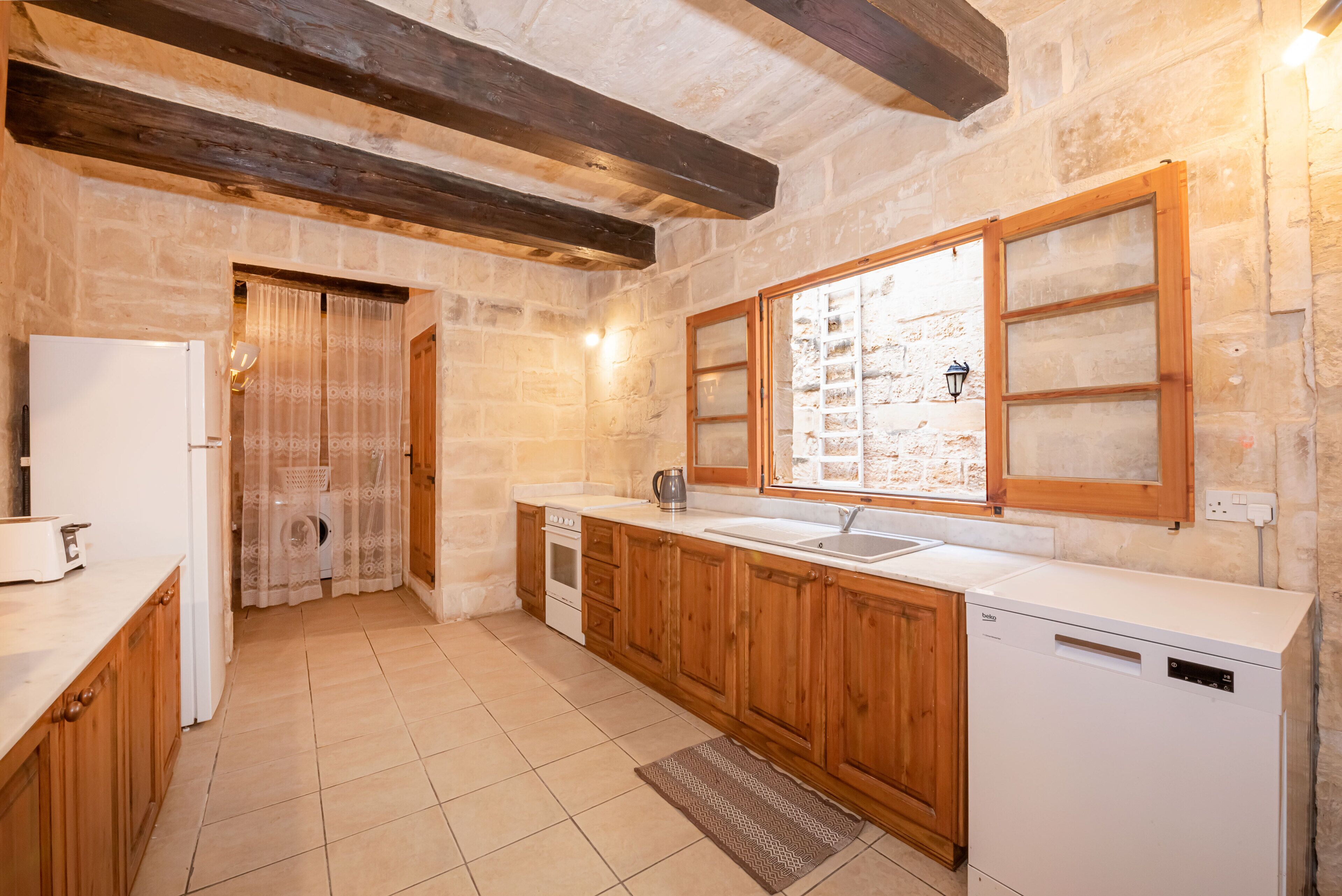 A kitchen with wooden cabinets, a white dishwasher, a sink, and a window with a view of the outside.