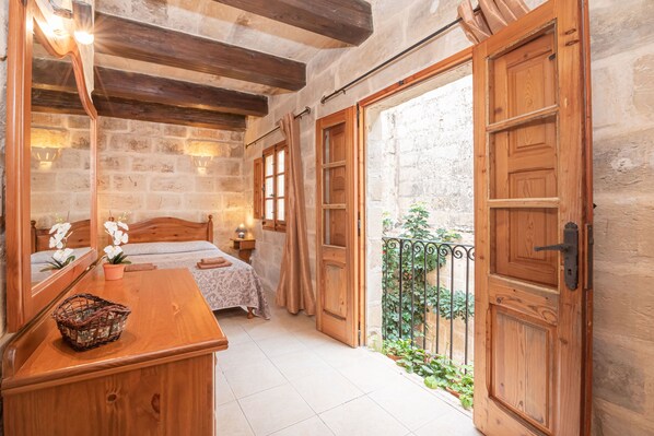 A bedroom with a wooden bed, a bedside table, a mirror, and a view of a courtyard.