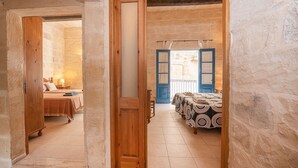 A bedroom with a wooden door, a bed with a patterned bedspread, and a view of another room through an open door. - 3 Bedrooms House of Character in Rabat Near Mdina - Casa Melita (Rabat)