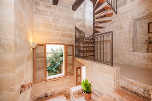 A stone staircase with a wooden handrail, a potted plant, and a window with a view of greenery.