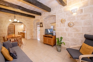 A spacious living area with a stone wall, wooden furniture, a television, and a dining table.