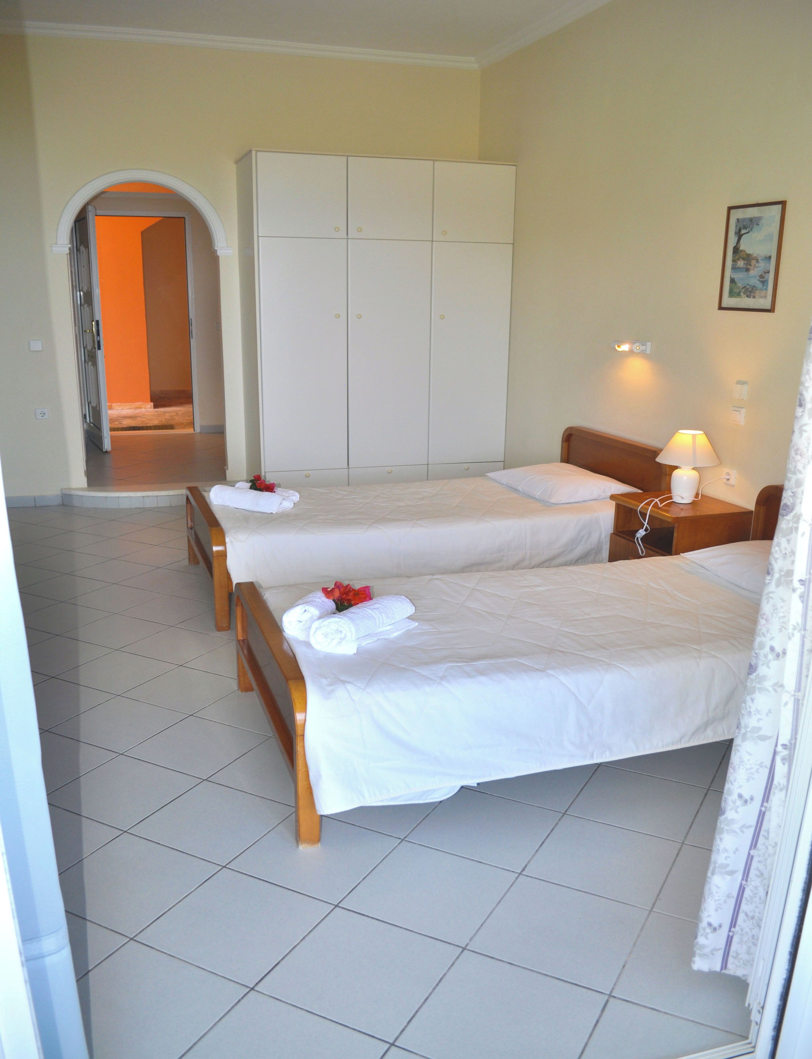 A hotel room with two beds, a wardrobe, a nightstand with a lamp, and a painting on the wall.