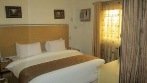 Une chambre d’hôtel avec un lit, une table de chevet, une lampe et une fenêtre avec des rideaux.