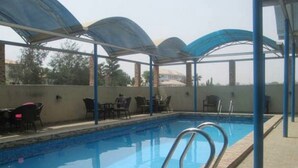 Une piscine extérieure dotée d’un espace détente couvert et de chaises.
