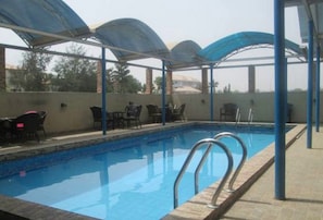 An outdoor swimming pool with a covered seating area and chairs. - Room-abuja Elomaz Hotel-guest Suite (Abuja)