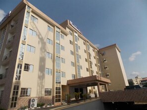 A multi-story hotel with a flat facade, large windows, and a covered entrance area with potted plants. - Room-abuja Elomaz Hotel-guest Suite (Abuja)