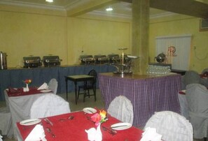 Un salón de banquetes con mesas dispuestas para comer, un escenario con micrófono y una zona de bufé.